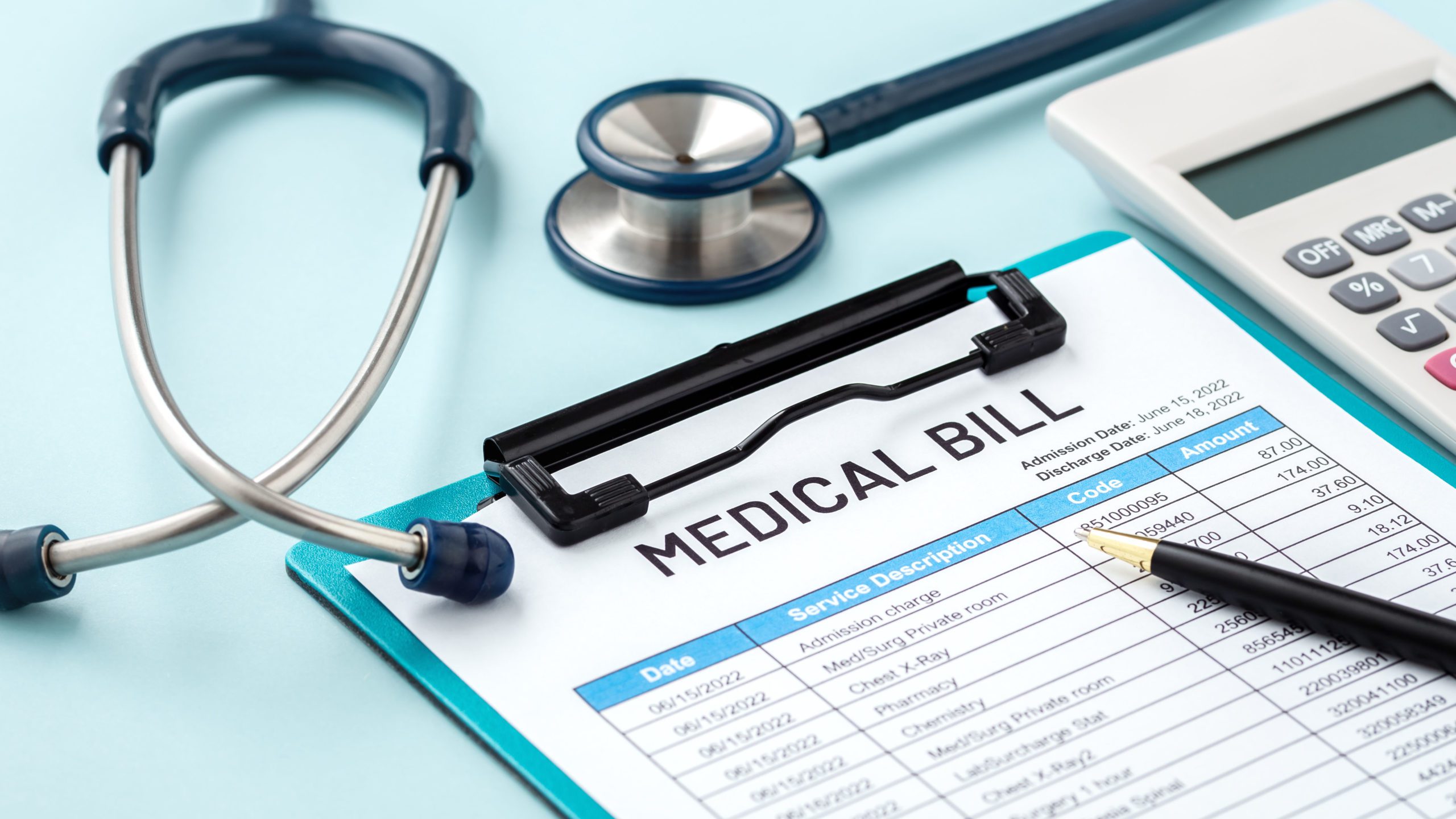 Medical bill on a clipboard with a stethoscope, calculator, and pen